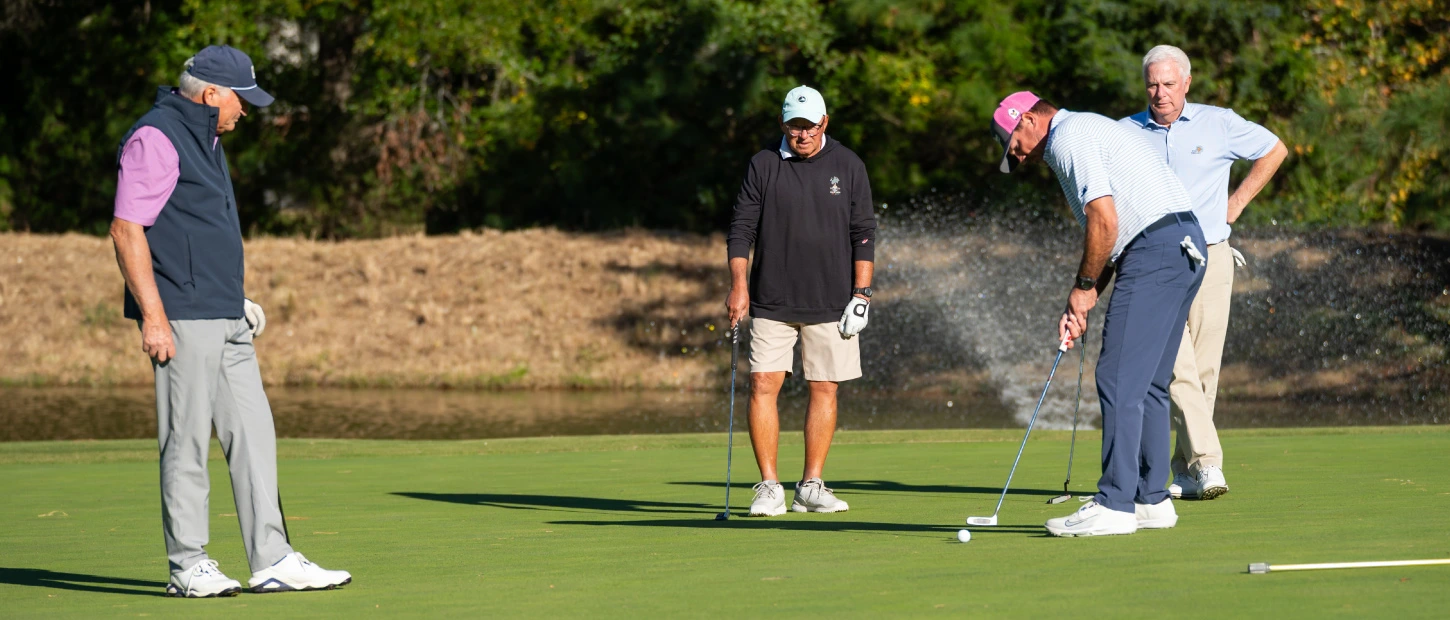 group of golfers on the green watching one putt