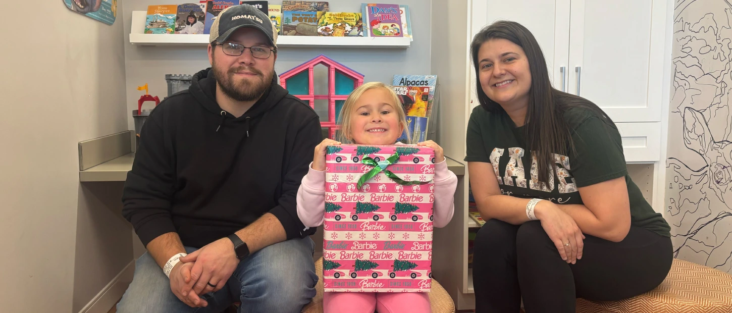 mother and father with their daughter holding a wrapped present